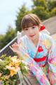 A woman in a kimono sitting on a bench with flowers.