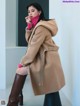 A woman in a beige coat and brown boots sitting on a stool.