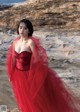 A woman in a red dress standing on a rock by the ocean.